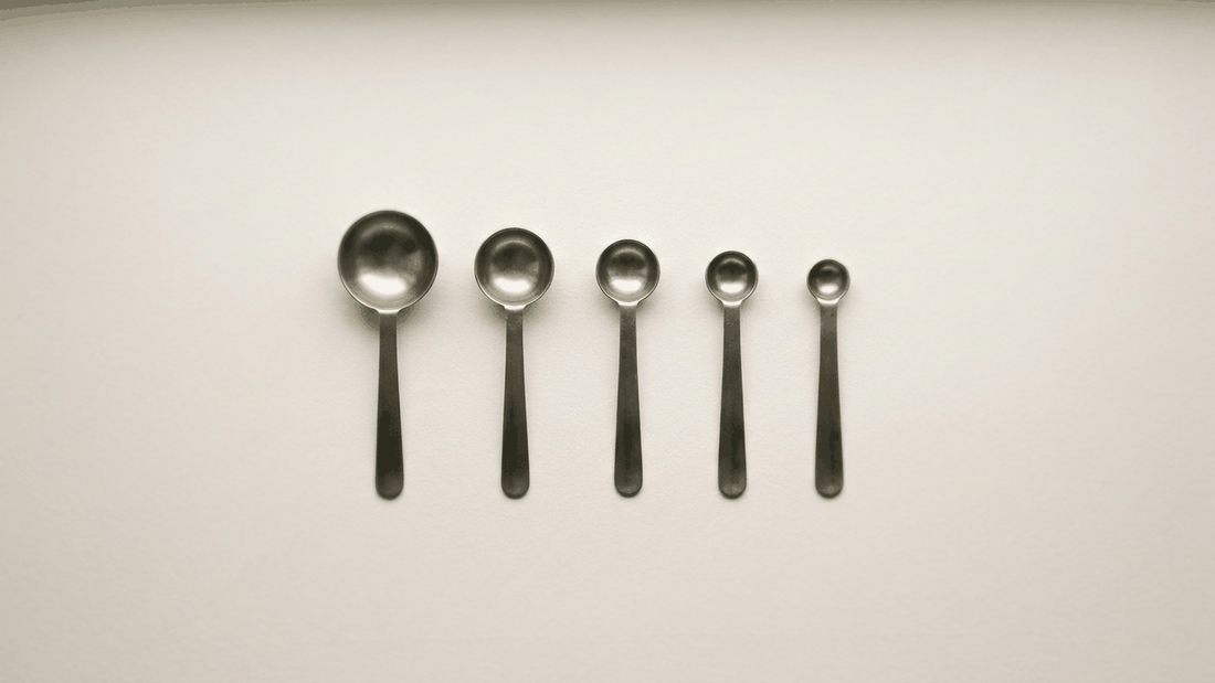 A set of five stainless steel measuring spoons laid in a row from largest to smallest on a plain off-white surface, photographed flat from above in even daylight.
