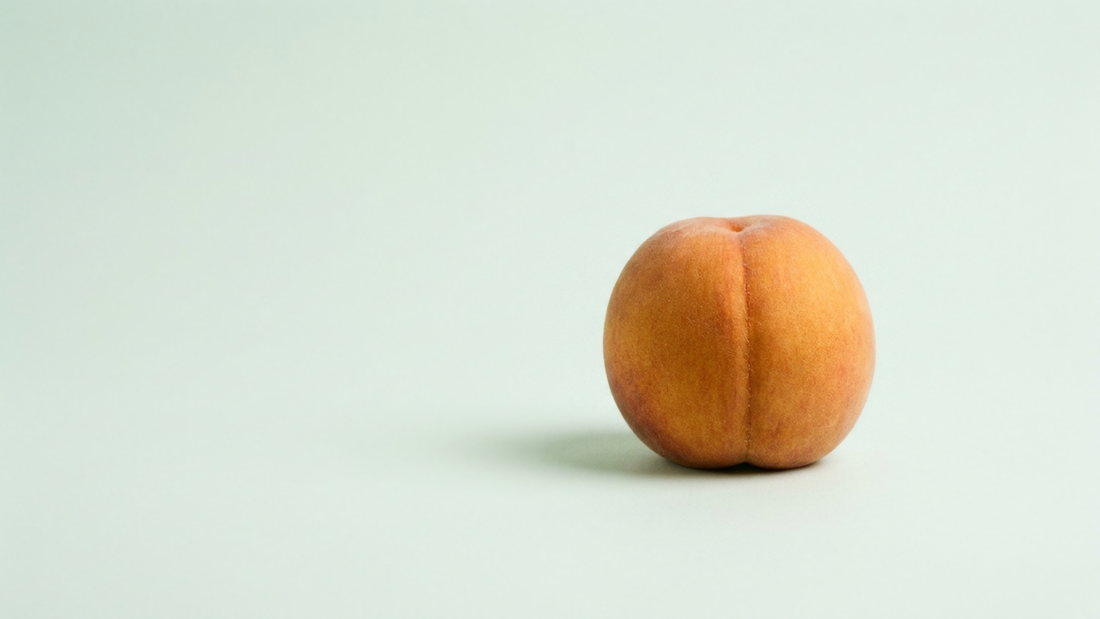 A single ripe peach, whole and alone on a seamless pale mint surface, photographed straight on in flat even daylight with a soft contact shadow.